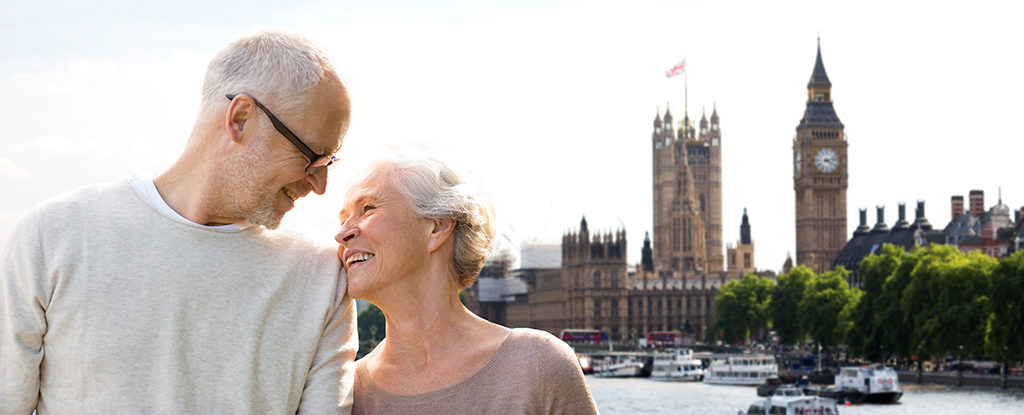 Couple with travel insurance for those over 65 standing on bridge with big ben in the background