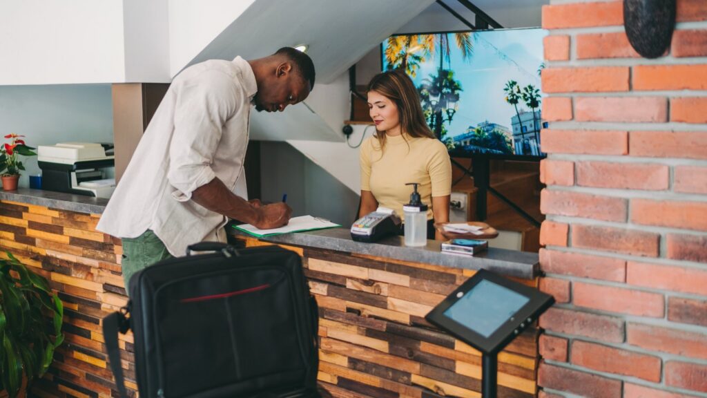 A traveler checking in at a hotel front desk while staff assists him with his stay