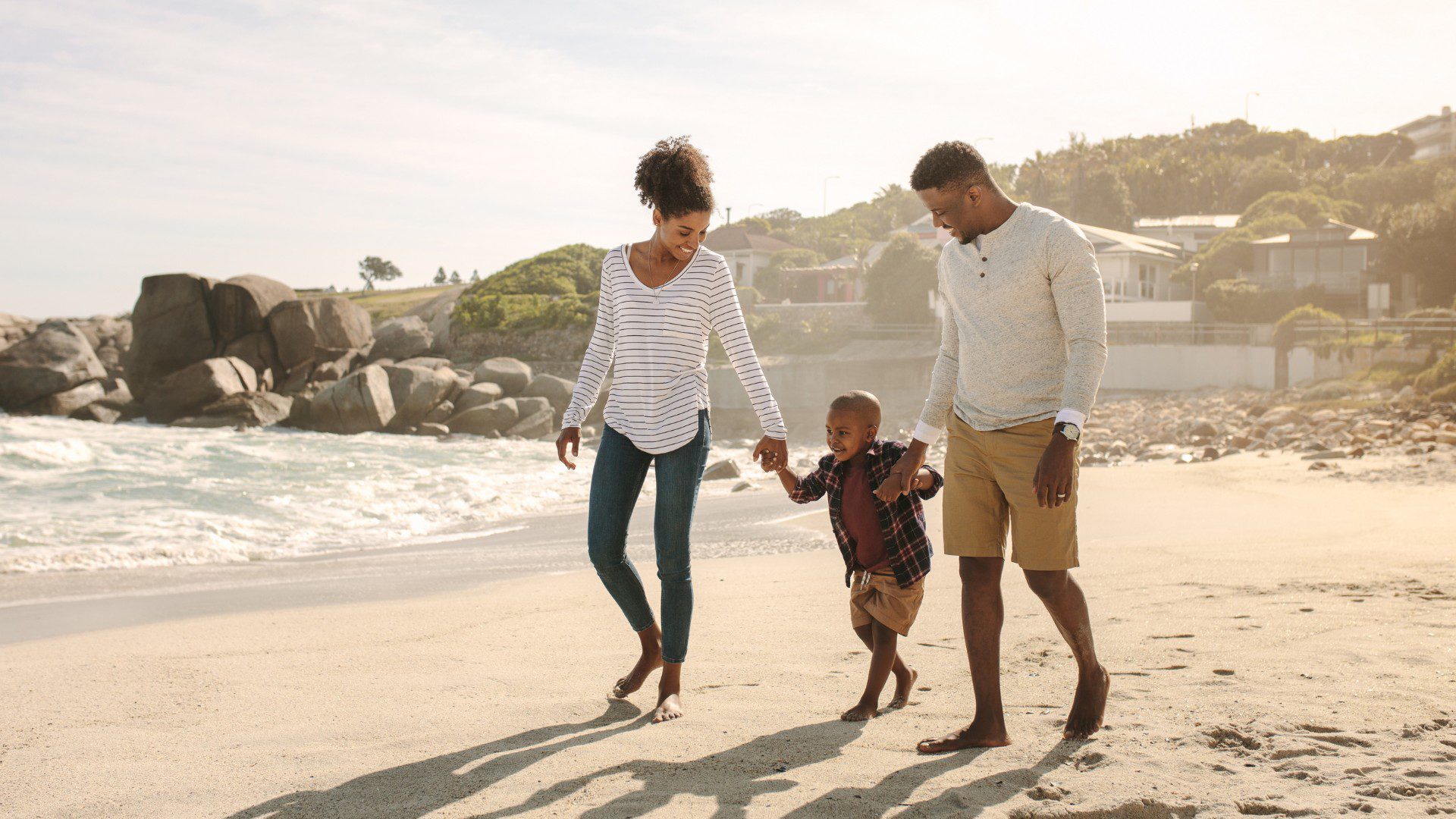 A family of three walking together outdoors on a beach.